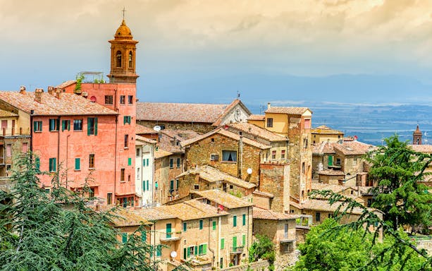 Val D’Orcia village with rustic buildings and a bell tower, Tuscany landscape in the background.