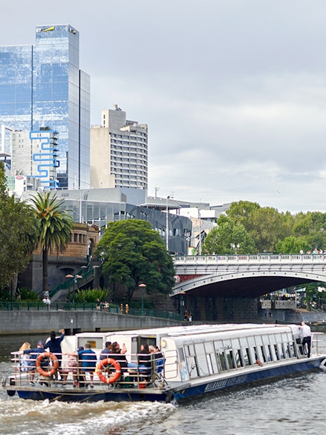 Cruise boat on Yarra River with Melbourne skyline and bridge in view.