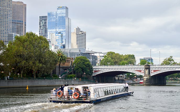 Cruise boat on Yarra River with Melbourne skyline and bridge in view.