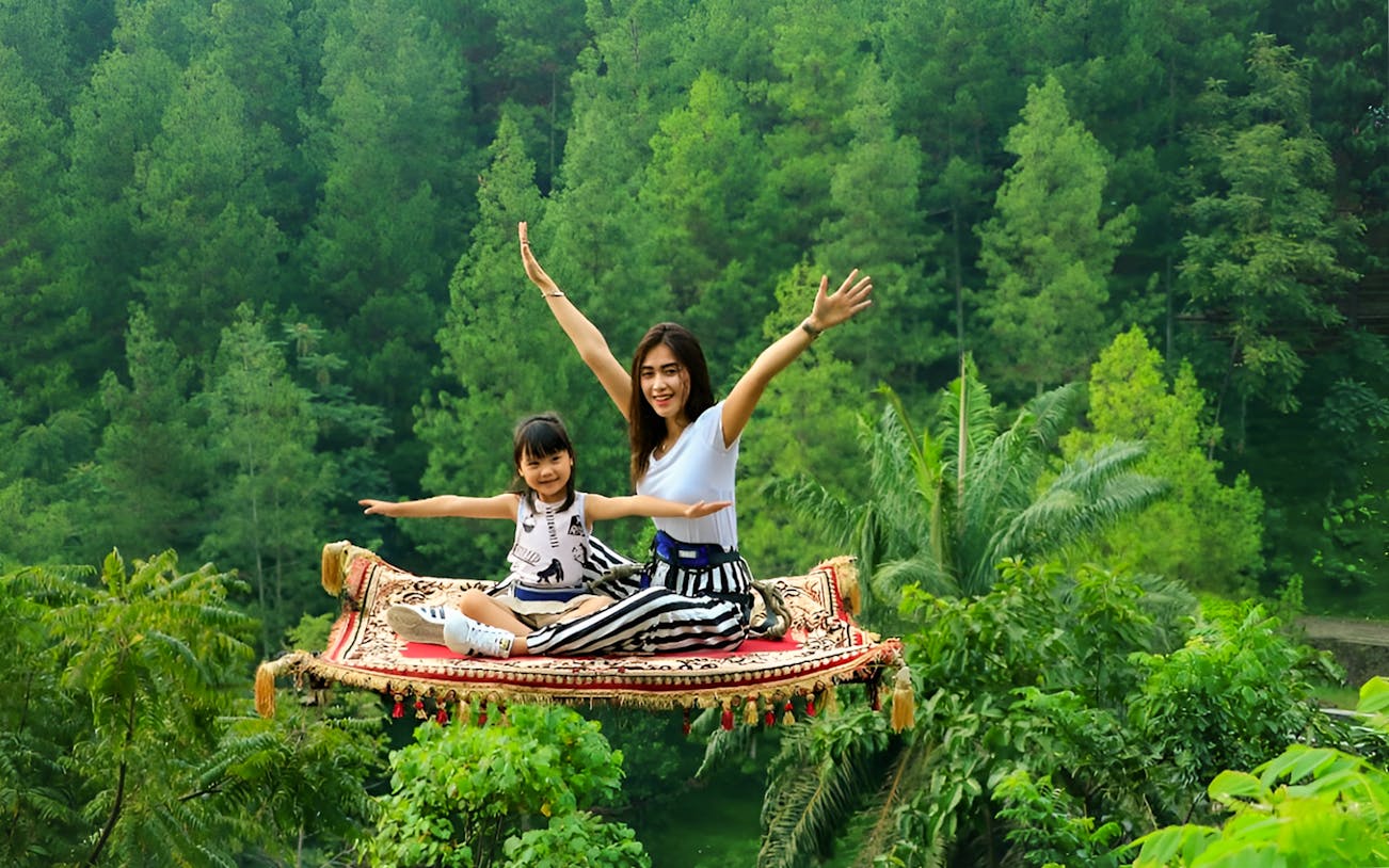 Visitors on a flying carpet ride at Dago Dreampark, surrounded by lush greenery.