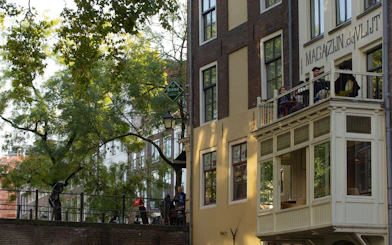 Utrecht canal-side building with balcony, trees, and people enjoying a walking tour.