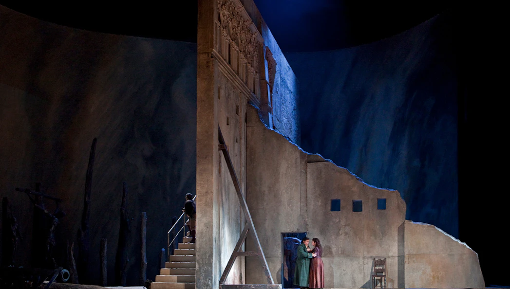 Opera scene from Il Trovatore with two performers on stage near a stone wall.