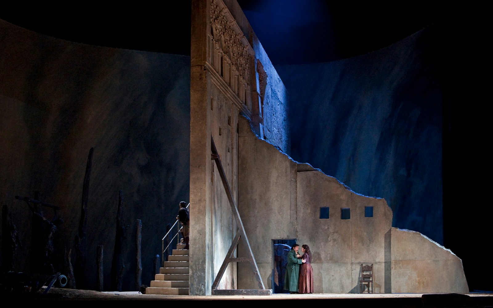 Opera scene from Il Trovatore with two performers on stage near a stone wall.
