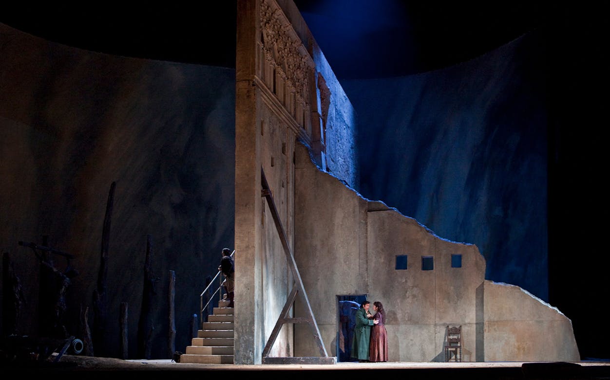 Opera scene from Il Trovatore with two performers on stage near a stone wall.