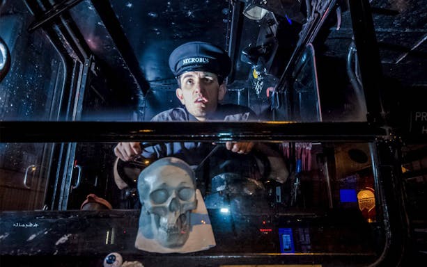 Bus driver in uniform steering a ghost-themed tour bus with a skull decoration.