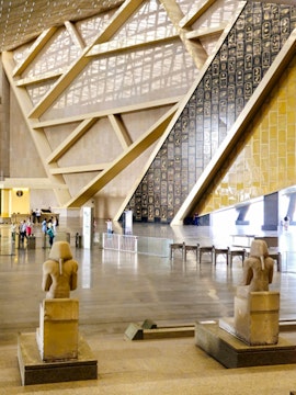 Interior of the Grand Egyptian Museum with statues and hieroglyphic wall.