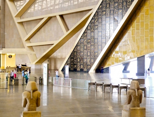 Interior of the Grand Egyptian Museum with statues and hieroglyphic wall.