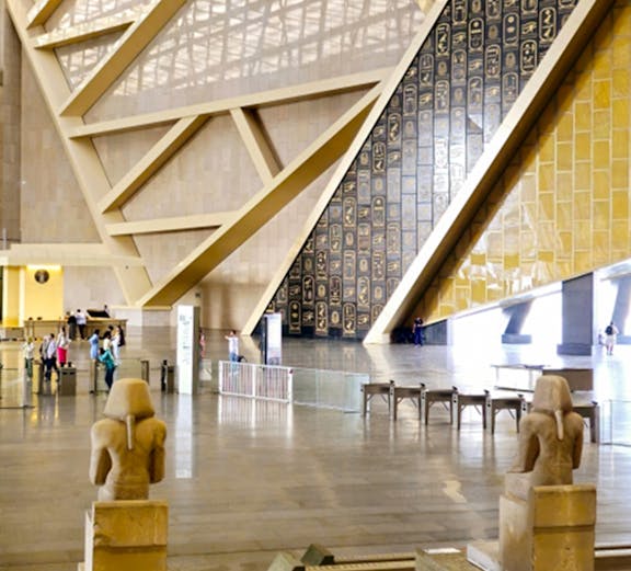 Interior of the Grand Egyptian Museum with statues and hieroglyphic wall.