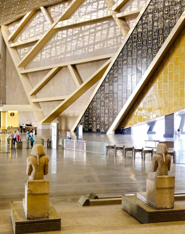 Interior of the Grand Egyptian Museum with statues and hieroglyphic wall.