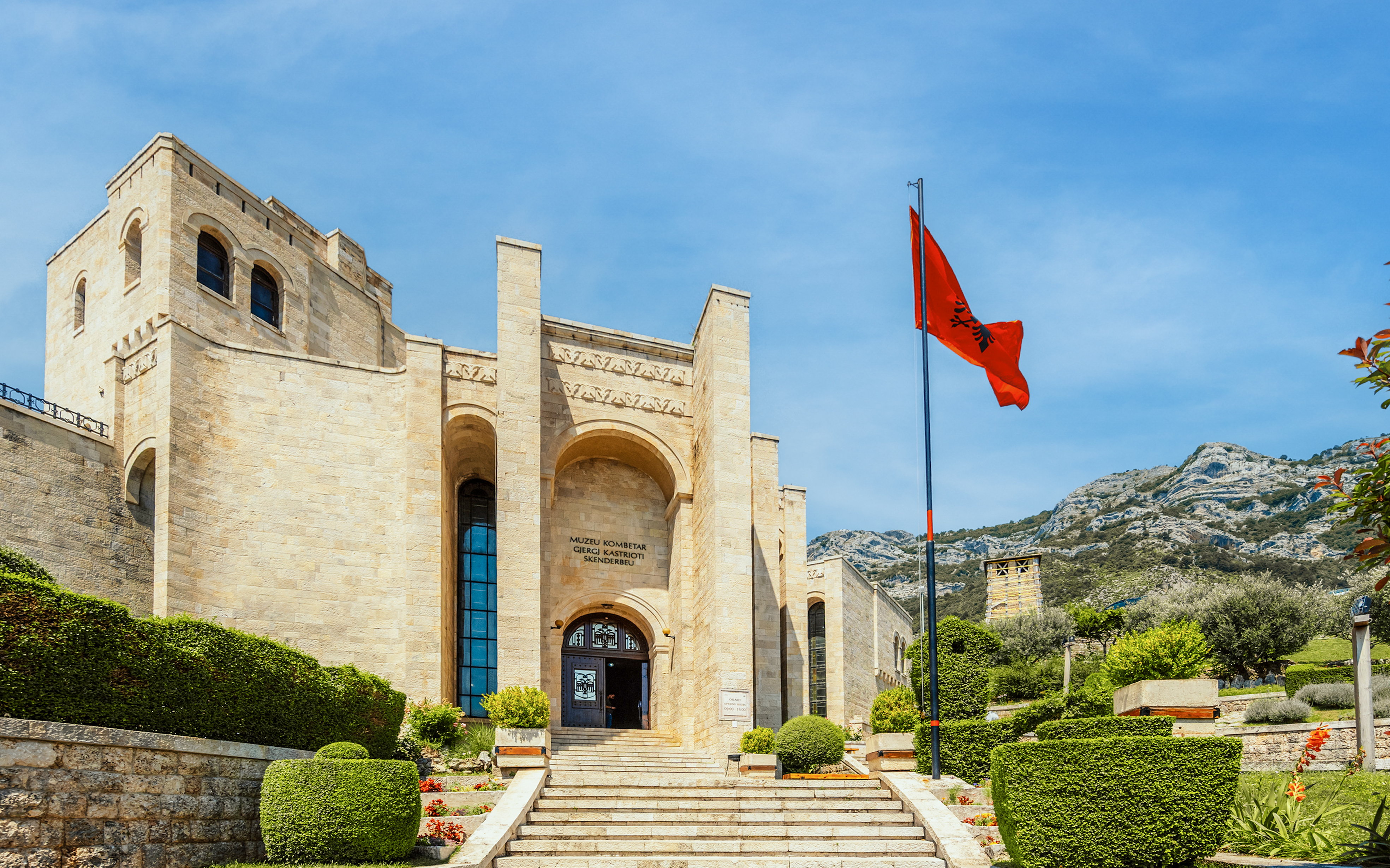 Castle Kruje entrance with Skanderbeg Museum, Kruje, Albania, featuring Albanian flag and mountain backdrop.