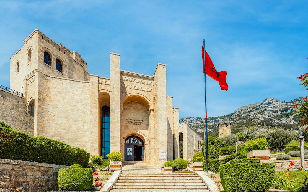 Castle Kruje entrance with Skanderbeg Museum, Kruje, Albania, featuring Albanian flag and mountain backdrop.