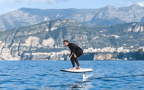 Person e-foiling on water with Capri cliffs in the background.