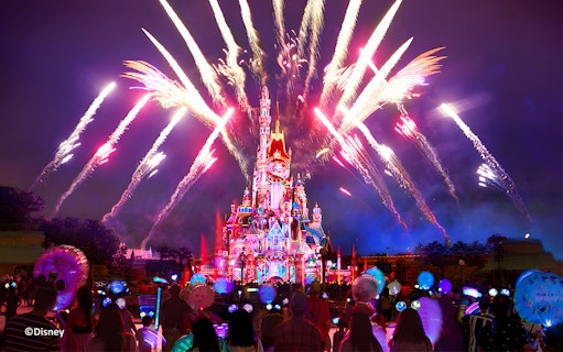 Fireworks over Hong Kong Disneyland castle at night with crowd watching.