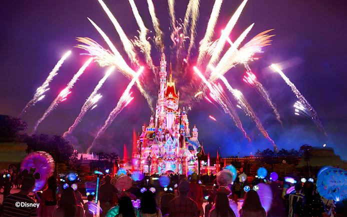 Fireworks over Hong Kong Disneyland castle at night with crowd watching.