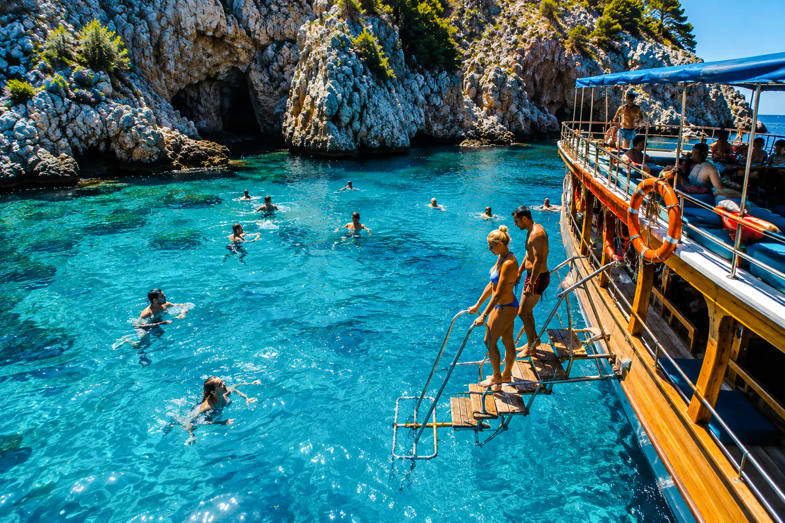 Tourists swimming near a boat in Alanya's clear blue waters.