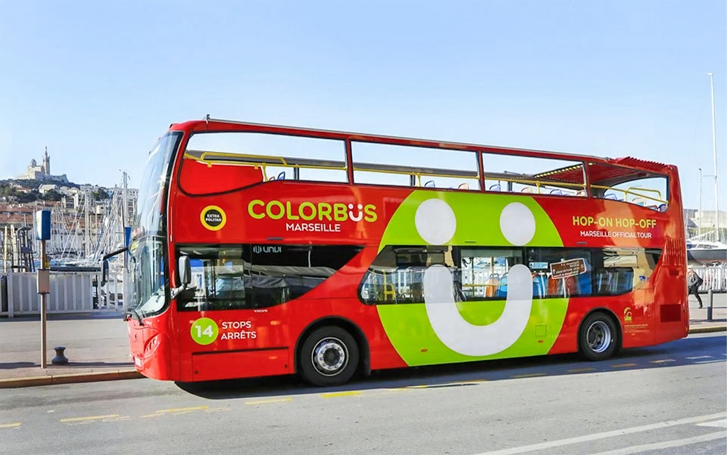 Colorful double-decker Colorbus in Marseille with Notre-Dame de la Garde in the background.