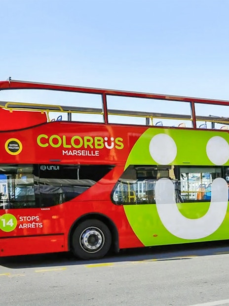 Colorful double-decker Colorbus in Marseille with Notre-Dame de la Garde in the background.