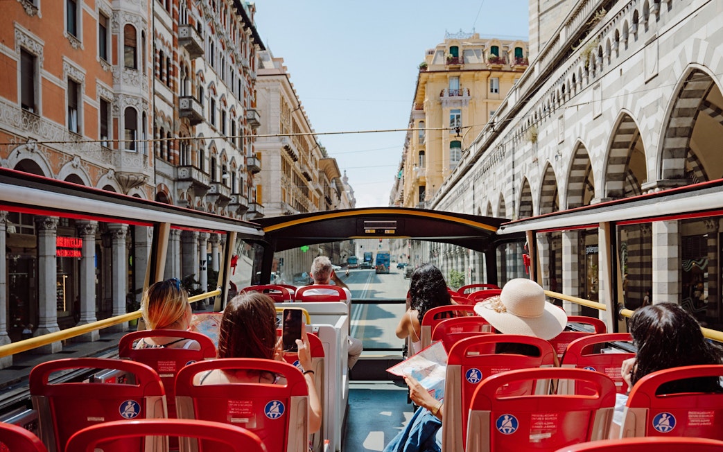 Passengers on a City Sightseeing bus tour through historic streets in Genova, Italy.