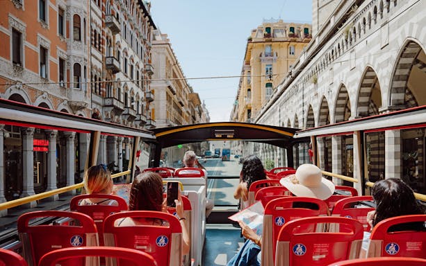 Passengers on a City Sightseeing bus tour through historic streets in Genova, Italy.