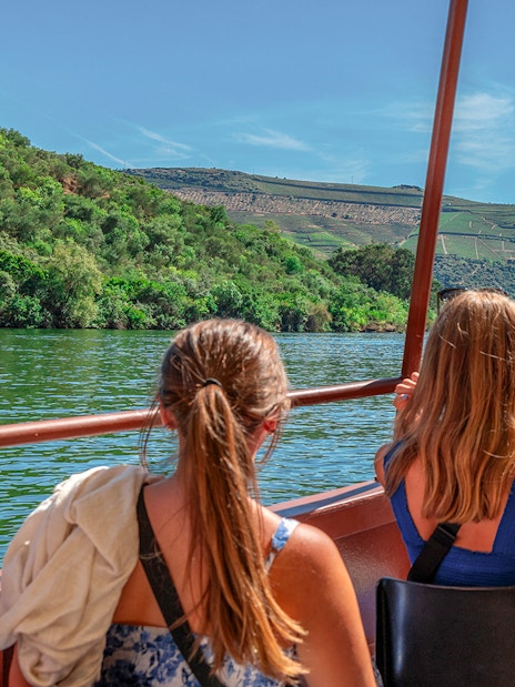 Tourists on a Douro River cruise boat, viewing lush vineyards near Porto.