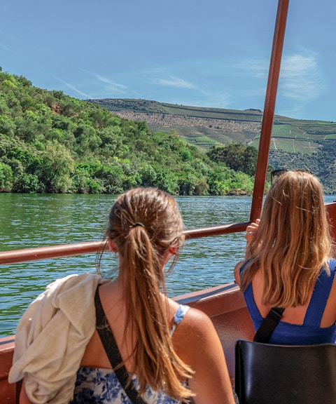 Tourists on a Douro River cruise boat, viewing lush vineyards near Porto.