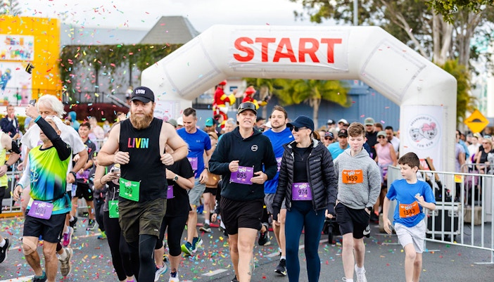 Participants in a fun run at Dreamworld, Gold Coast, wearing colorful outfits and running past theme park attractions.