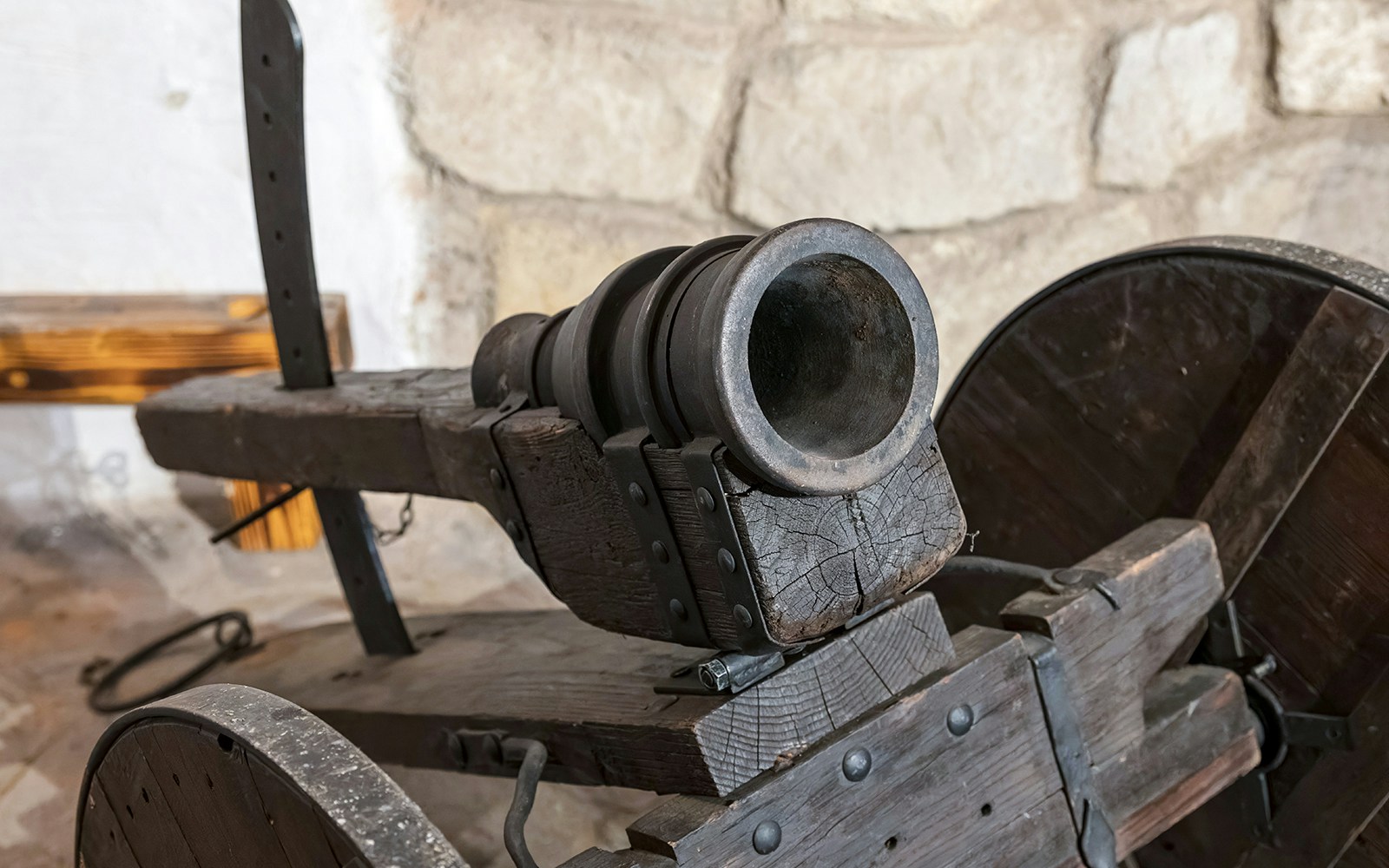 Portable cannon on display at a museum with stone wall background.