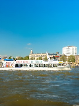 River cruise boat on Rotterdam's waterway with cityscape in the background.