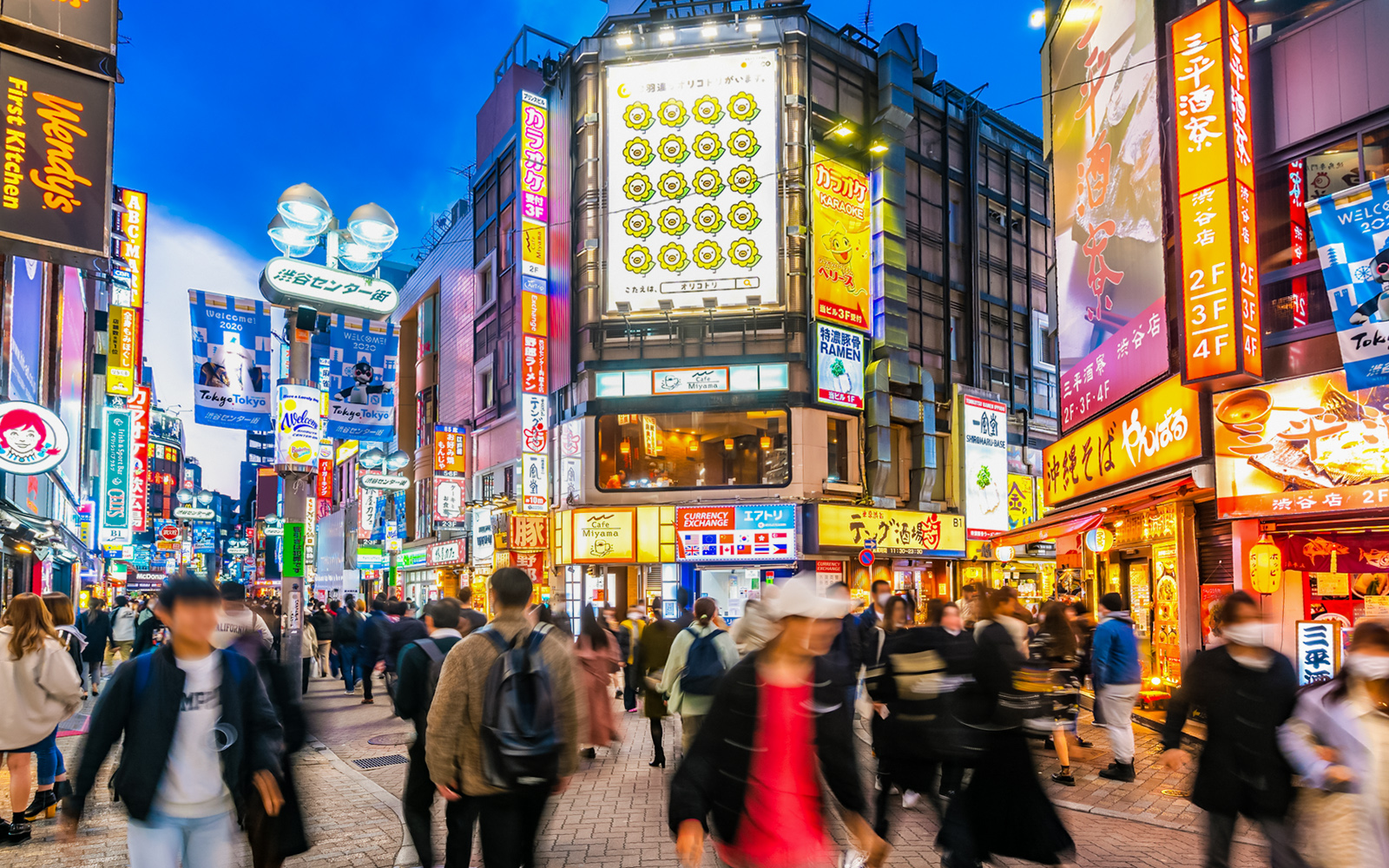 Shibuya Crossing bustling with tourists under neon lights in Tokyo, Japan.