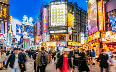 Shibuya Crossing bustling with tourists under neon lights in Tokyo, Japan.