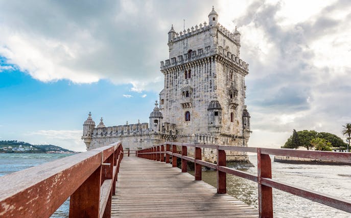 Belem Tower in Lisbon, Portugal, viewed from a wooden walkway over the Tagus River.