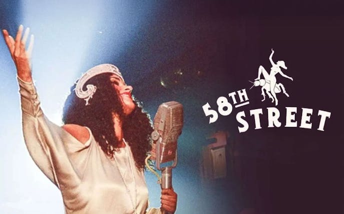 Performer singing on stage with vintage microphone, 58th Street logo in background.