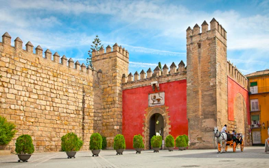 Tourists in a horse-drawn carriage outside Alcazar of Seville's entrance.