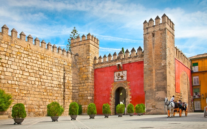 Tourists in a horse-drawn carriage outside Alcazar of Seville's entrance.