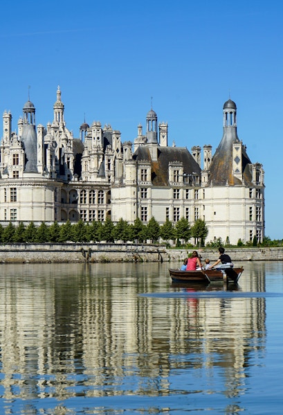 Rowboat on river with view of Château de Chambord, Loire Valley, France.