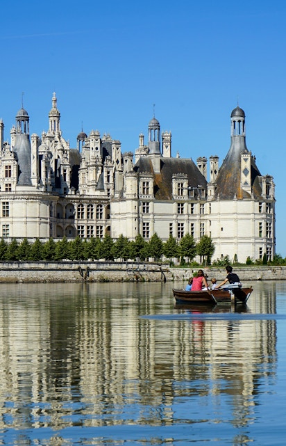 Rowboat on river with view of Château de Chambord, Loire Valley, France.