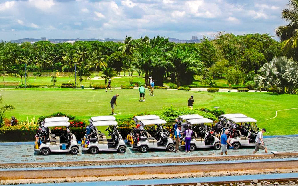 Golfers on the green at Batam Island Country Club with golf carts nearby.