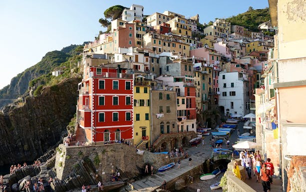 Colorful cliffside village of Riomaggiore in Cinque Terre, Italy, with boats and tourists exploring.