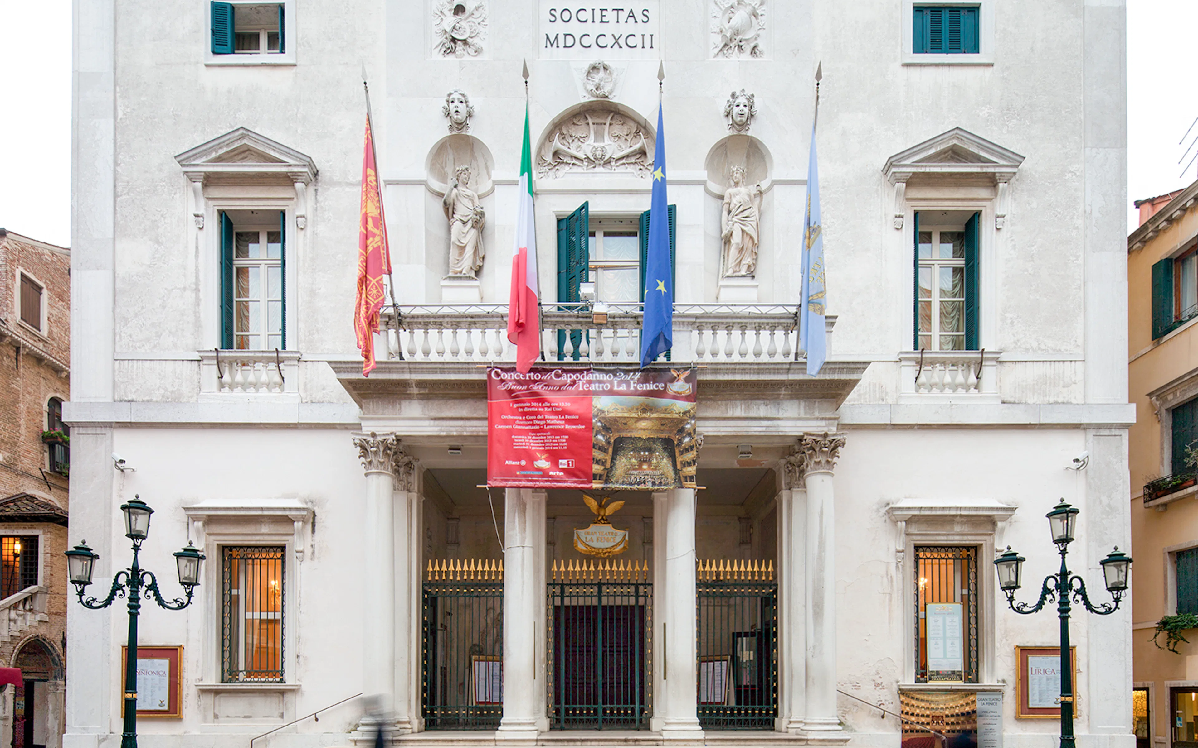 Facade of Teatro La Fenice in Venice with flags and classical statues.