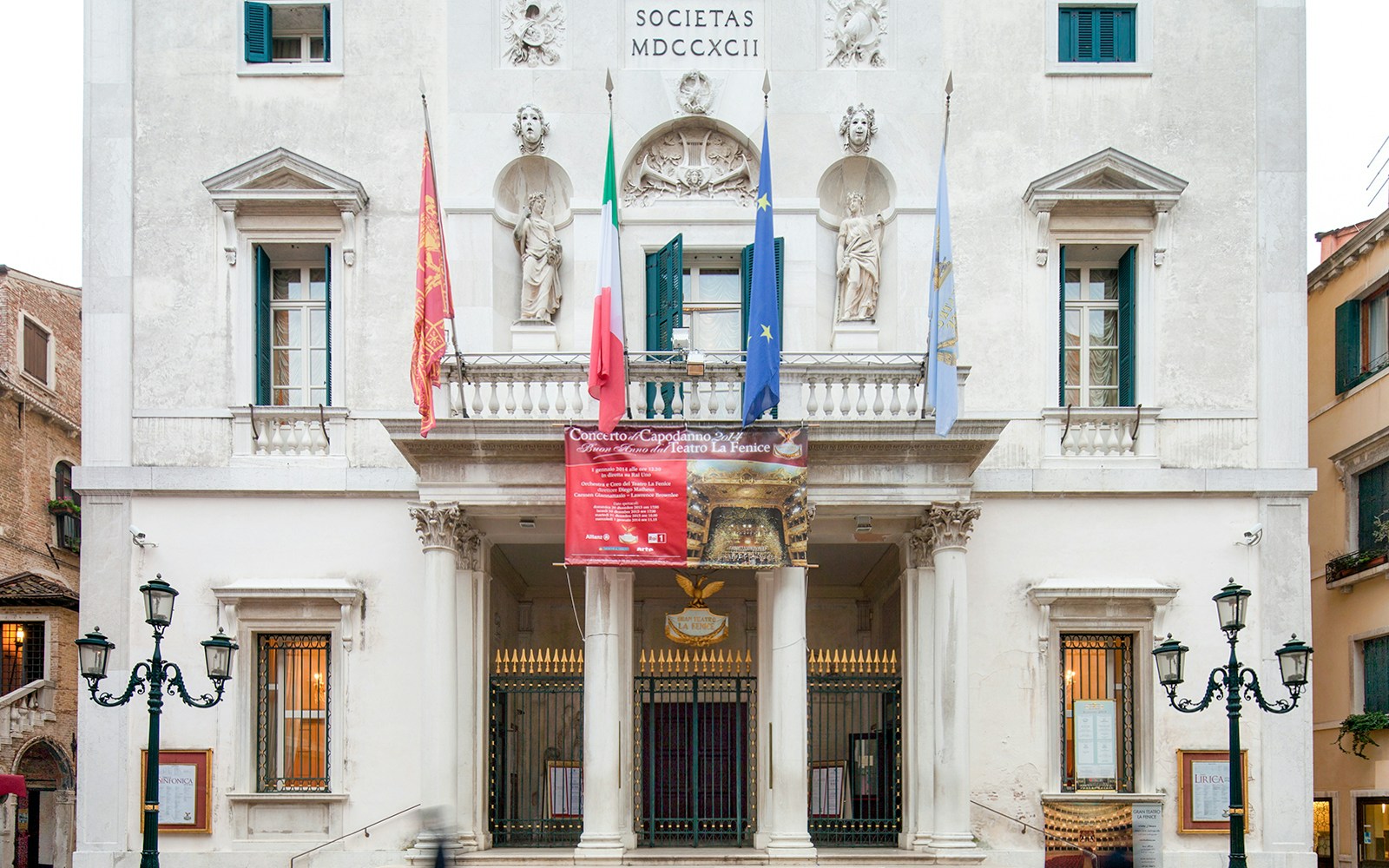 Facade of Teatro La Fenice in Venice with flags and classical statues.