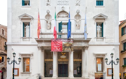 Facade of Teatro La Fenice in Venice with flags and classical statues.