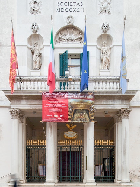 Facade of Teatro La Fenice in Venice with flags and classical statues.