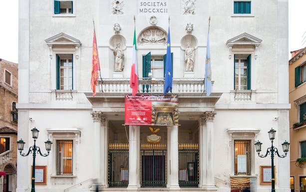 Facade of Teatro La Fenice in Venice with flags and classical statues.