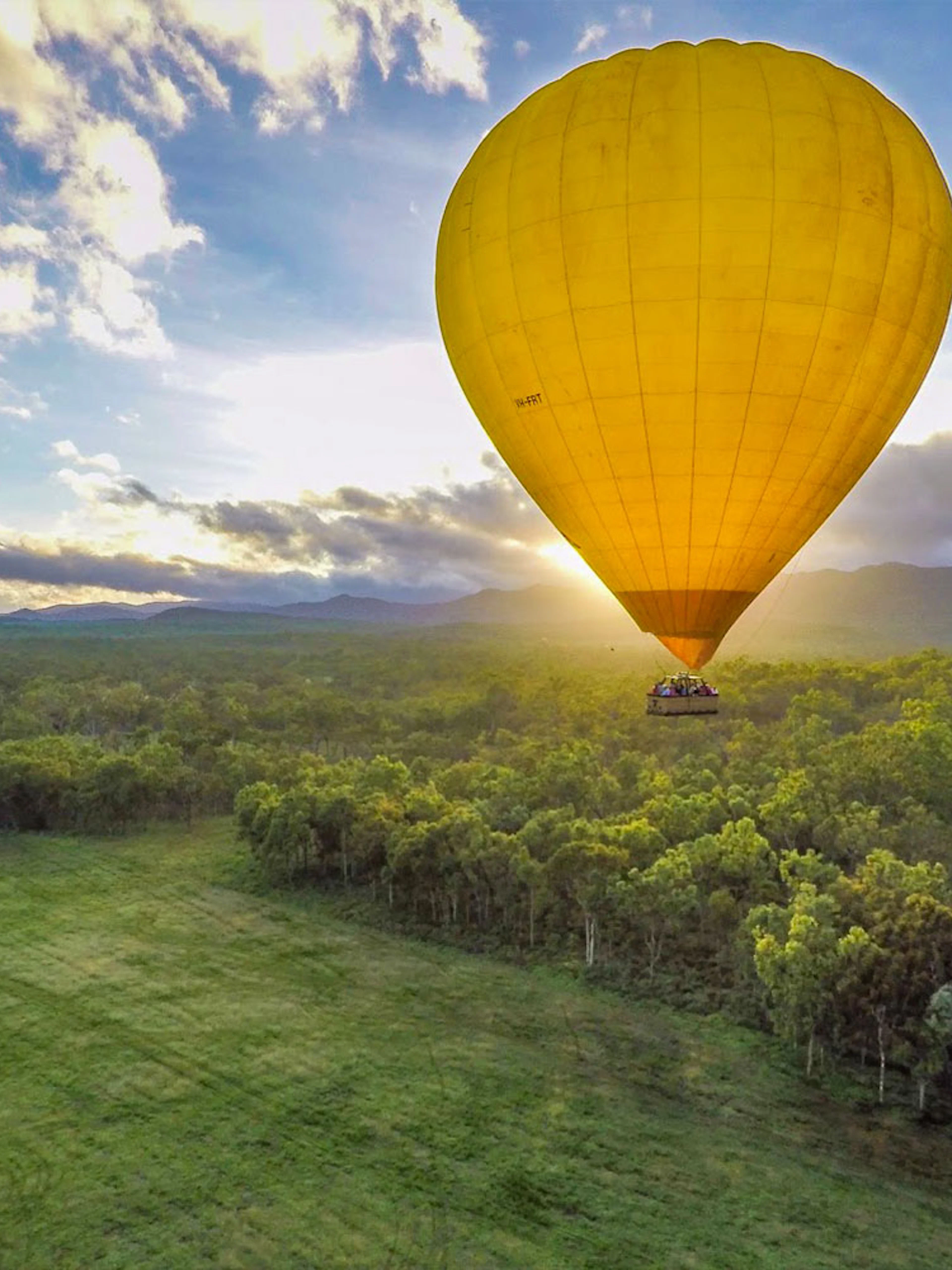 Hot air balloon over lush landscape at sunrise in Cairns, Australia.