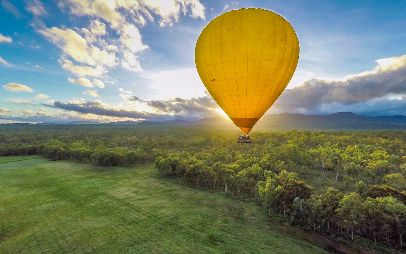 Hot air balloon over lush landscape at sunrise in Cairns, Australia.