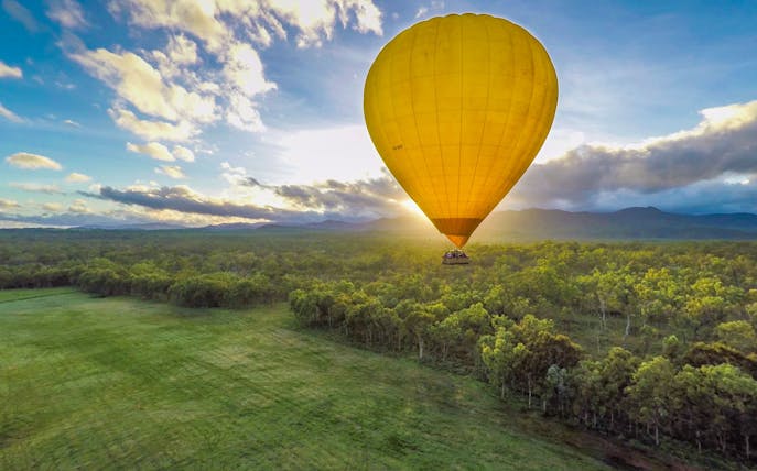 Hot air balloon over lush landscape at sunrise in Cairns, Australia.
