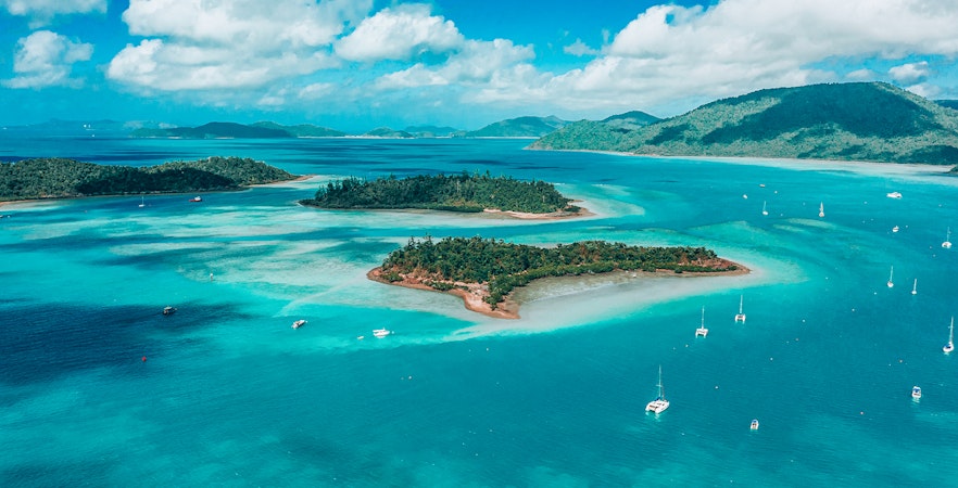 Skydiver descending over Airlie Beach coastline, Queensland, with ocean and islands in view.