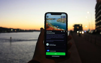 Hand holding a phone displaying Porto by the Ocean city exploration game at sunset by the water.