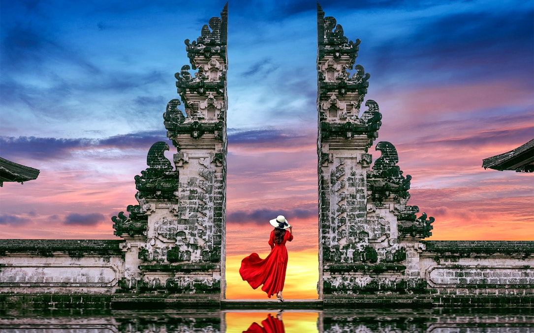 Woman in red dress at Bali's Lempuyang Temple gates during sunrise.