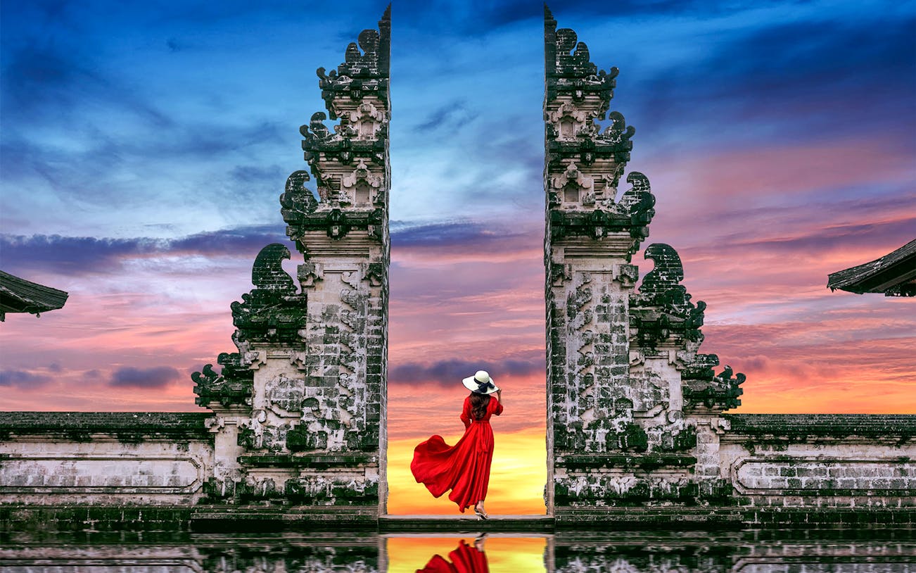 Woman in red dress at Bali's Lempuyang Temple gates during sunrise.